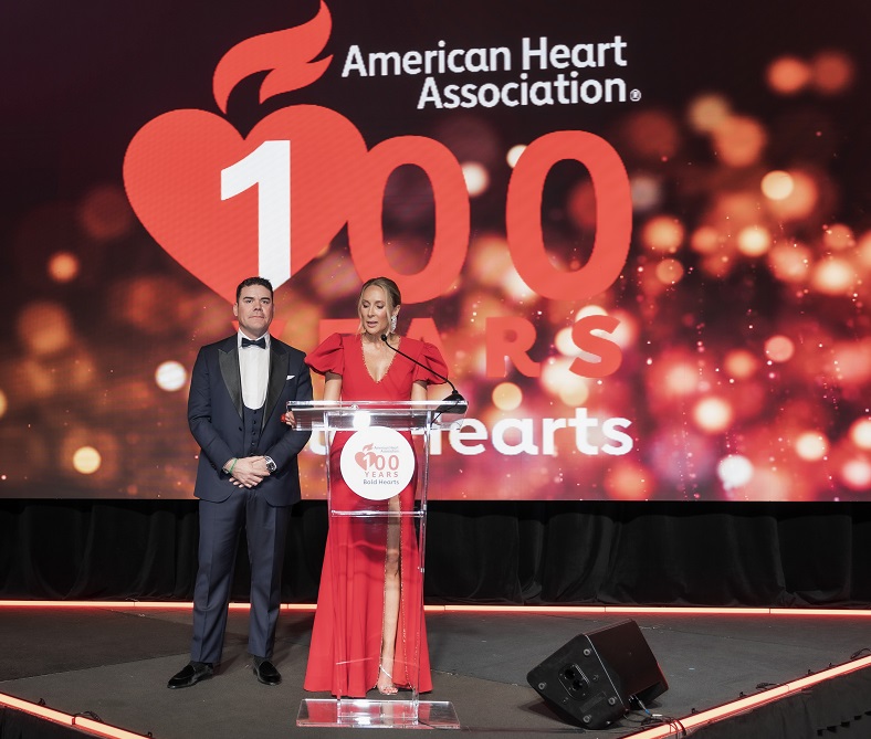 Man and woman at podium in front of American Heart Association 100 years bold hearts logo